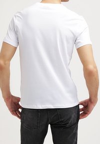 Bílá bavlněná tričko s krátkým rukávem a kulatým výstřihem, které má jednoduchý design a mírnou elasticitu pro pohodlí.