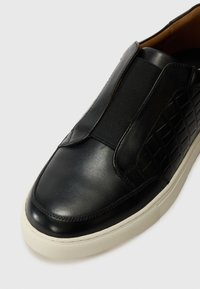 Crne kožne cipele bez vezanja s elastičnim bočnim panelima, teksturiranim akcentima, zaobljenim vrhom i bijelim gumenim potplatom. Glatka završna obrada i elegantan dizajn.