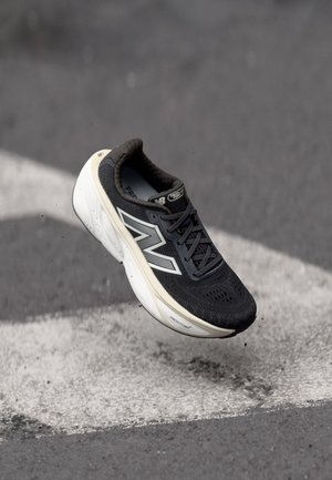 Schwarzer Sportschuh mit einem Obermaterial aus Netzgewebe, weißem Logo und cremefarbener Zwischensohle. Verfügt über eine gepolsterte Einlegesohle und perforierte Details für Atmungsaktivität.