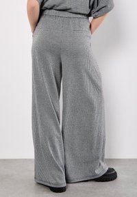 Breda byxor i ett texturerat tyg med ett monokromt rutmönster. Har ett elastiskt midjeband och sidofickor. Svarta plattformsskor.