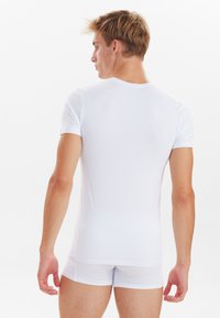 Witte t-shirt met korte mouwen van gladde stof, aansluitend ontwerp, toont de rug en schouders van een persoon die bijpassende witte shorts draagt.