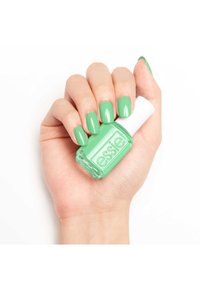 Vernis à ongles vert dans une bouteille en verre transparent avec un capuchon blanc, tenu dans une main avec des ongles soigneusement manucurés peints dans la même teinte de vert.