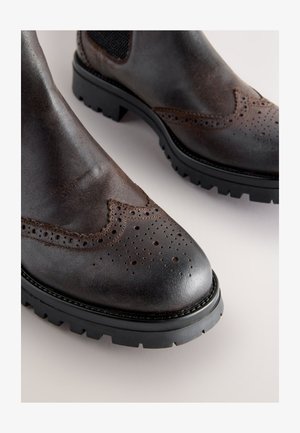 Donkere bruine leren enkellaarsjes met brogue-details, een licht spits toelopende neus en een robuuste zwarte rubberen zool. Gestructureerd oppervlak bij de veteropening.