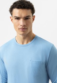 Langarmhemd aus hellblauem Stoff mit rundem Ausschnitt und linke Brusttasche. Glatte Textur und taillierter Schnitt.