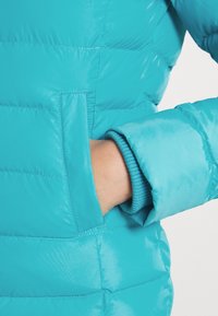 Turquoise donsjack met een ritssluiting aan de zak, geribbelde manchetten en een glanzende afwerking, met de nadruk op een lichtgewicht en geïsoleerd ontwerp.