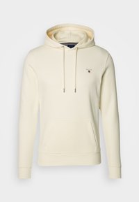 Sudadera color crema hecha de una tela suave, con un bolsillo frontal, capucha con cordón y un pequeño logo bordado en el pecho.