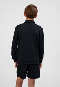 Svart sweatshirt med texturerad yta, med krage och detaljering på axlarna. Matchas med svart shorts i samma material.