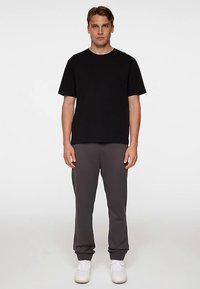 Musta lyhythihainen T-paita, yhdistettynä harmaisiin collegehousuihin, molemmat pehmeästä kankaasta, väljällä mitoituksella ja joustavilla resoreilla.