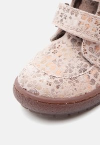 Chaussure à lanière en velcro en suède rose clair avec des motifs floraux. Bout rond, semelle texturée et légère brillance sur le design floral.