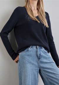 Pull en maille bleu marine avec col en V et manches longues, accompagné d'un jean bleu clair à jambes droites, texture lisse et détails de coutures minimaux.