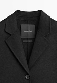 Cappotto in misto lana nero con colletto a rotondo, chiusura con un bottone e etichetta firmata all'interno. Tessuto morbido con un design classico.