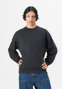 Mørk grå crewneck sweatshirt i et mykt stoff, med ribbede mansjetter og kant. Kombinert med lyseblå denimbukser med en avslappet passform.