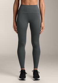 Leggings sportivi a vita alta di colore grigio scuro con una texture liscia e un design senza cuciture, abbinati a scarpe da ginnastica nere.
