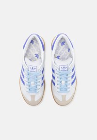 Vita sneakers med blå ränder, ljusblå snören och gummigummi-sula; har en texturerad, märkesinläggssula och en tåkappa av mocka.