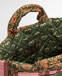 Intérieur du sac matelassé vert avec des motifs floraux en orange et rose. Comprend une poche zippée et des étiquettes de marque. Design en tissu robuste et texturé.