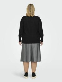 Melna adīta džemperis, pelēka satīna svārki un melni sporta apavi. Džemperim ir brīvs piegriezums, kamēr svārkiem ir gluda virsma un izplestā forma.