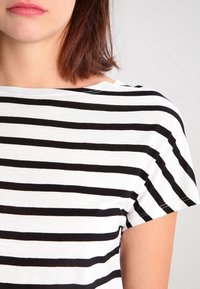 Sort og hvid stribet t-shirt, korte ærmer, rund halsudskæring, lavet af blødt bomuldsmateriale, der viser et ujævnt stribet mønster.