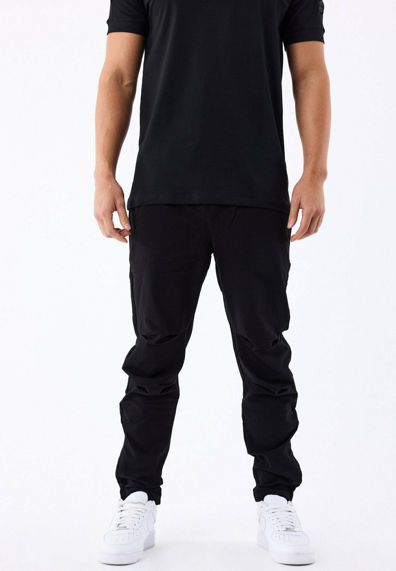 Pantalon cargo noir à coupe décontractée, avec de multiples poches et une texture de tissu lisse, associé à des baskets blanches.