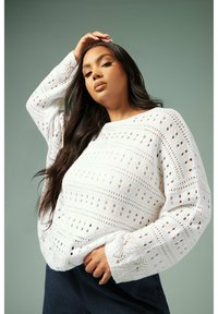 Vit stickad tröja med genombrutna mönster, vida ärmar och en avslappnad passform. Den strukturerade tyget ger ett lätt och luftig utseende.