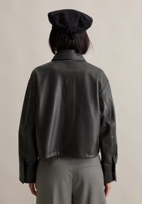 Schwarze Lederjacke mit cropped Design, klassischem Kragen, subtiler Textur und gesteppten Akzenten; getragen mit grauen gestreiften Hosen.