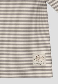 Grau- und cremefarben gestreifter Stoff, gerippte Textur, mit einem Patch im Igel-Design und einem "Cutness Club"-Etikett am Saum.