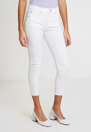 Jean capri en denim blanc avec un design ajusté, un ourlet effiloché et des poches avant, associés à des chaussures à talons blocs blanches.