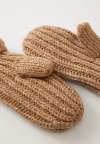 Moufles tricotées en beige chaud. Laine épaisse avec une texture côtelée. Présente une forme arrondie et une section pour le pouce sur chaque moufle.