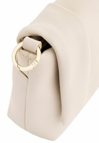 Beżowa skórzana kopertówka o złożonym designie, z akcentem w postaci złotego metalowego pierścienia. Gładka tekstura z widocznymi detalami szwów.