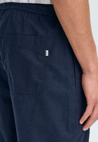 Marineblaue Hosen aus leichtem Stoff, mit elastischem Bund, seitlichen Taschen und einer aufgenähten Tasche auf der Rückseite.
