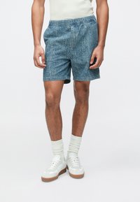 Szorty dżinsowe w wyblakłym niebieskim odcieniu, z elastycznym paskiem w talii i bocznymi kieszeniami, zestawione z białymi trampkami i jasnymi skarpetkami.