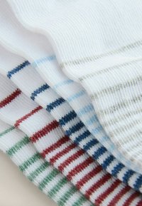 Pile de chaussettes blanches en tricot avec des fines rayures horizontales vertes, rouges, bleu foncé, bleu clair et grises, superposées.
