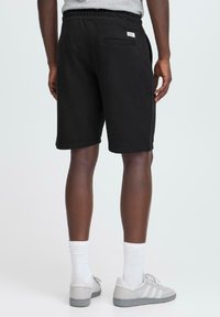 Pantalones cortos de sudor negro con cintura elástica y bolsillo trasero. Hechos de una tela suave, con una textura lisa y un diseño a la altura de la rodilla.