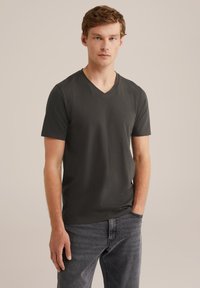 Sötét szürke V nyakú póló, puha anyagból, rövid ujjú, testhez álló fazonnal, sötét farmernadrággal párosítva. Zökkenőmentes textúra és egyszerű stílus.