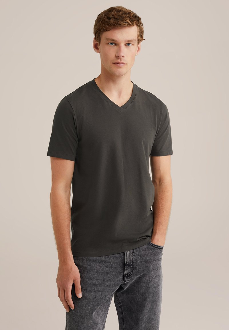 Sötét szürke V nyakú póló, puha anyagból, rövid ujjú, testhez álló fazonnal, sötét farmernadrággal párosítva. Zökkenőmentes textúra és egyszerű stílus.