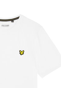 Witte katoenen t-shirt met een ronde hals en korte mouwen, versierd met een klein geel en zwart arendlogo op de linkerborst.