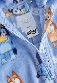 Pigiama in pile morbido e blu con zip, decorato con personaggi dei cartoni animati. Il tessuto è testurizzato e peloso, con tocchi di blu chiaro e scuro.