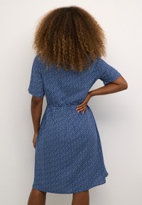 Modra kratka obleka s kratkimi rokavi in cvetličnim vzorcem, zategnjeno pasom in ohlapno krilo. Material se zdi lahkoten z gladko teksturo.