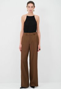 Mustat ribbed-halter-topit, joissa on kultaketjuakcentti; korkeavyötäröiset ruskeat leveälahkeiset housut; sileä kangas; malli seisoo pystyssä tasaista taustaa vasten.