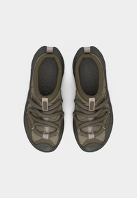 Ζευγάρι αθλητικά παπούτσια δέσιμου τύπου σε ελιά πράσινο και μαύρο χρώμα με επενδεδυμένες γλώσσες, από επάνω σε άσπρο φόντο.