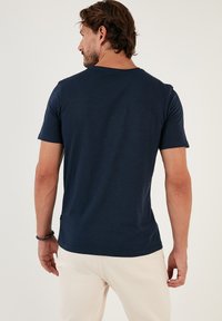 Tricou bleumarin cu mânecă scurtă, fabricat dintr-un material moale, având un guler rotund, croială normală și o textură subtilă. Design simplu, fără modele.