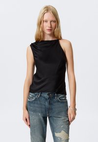 Top sans manches noir en tissu lisse, avec un décolleté drapé. Assorti à un jean bleu déchiré avec des motifs irréguliers.