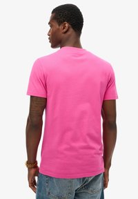 T-shirt rosa in cotone a maniche corte con una vestibilità classica, collo rotondo e senza loghi visibili, indossata con pantaloni corti in denim blu.