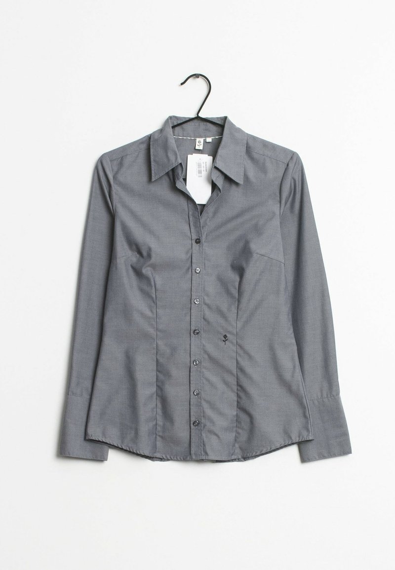 Chemise grise à boutons avec des manches longues, col classique et boutons noirs. Présente une poche sur le devant et un détail brodé subtil sur le côté gauche.