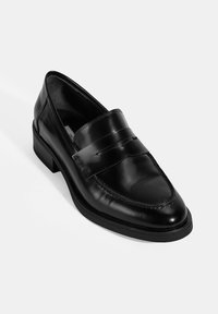 Schwarzer Leder-Loafer mit glänzender Oberfläche, ausgestattet mit einem gerippten Riemen und Kontrastnähten, auf einer niedrigen, glatten Sohle.
