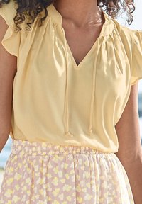 Gul blus med V-ringning, rynkade axlar och dragsnöre. Kombinerad med en rosa kjol med vita och gula blommönster.