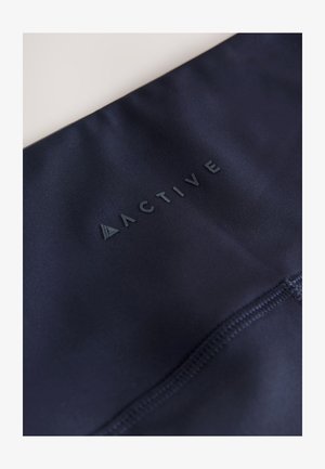 Marineblauwe sportkleding met een gladde textuur, voorzien van een verhoogd "ACTIVE" logo in een contrasterende donkere tint en zichtbare stikseldetails.