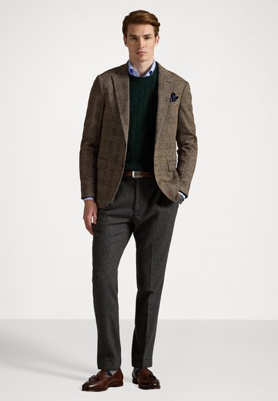Blazer marrón de pata de gallo sobre un suéter de punto con cable verde, pantalones de vestir grises, cinturón marrón y mocasines marrones, con una camisa azul debajo.