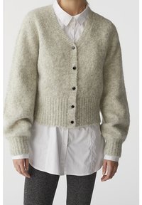 Cardigan de punto gris claro y difuso con escote en V, dobladillo acanalado y botones negros, superpuesto a una camisa blanca con botones.