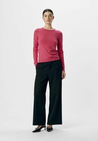 Top de punto de manga larga rosa combinado con pantalones de pierna ancha negros y tacones negros con abertura trasera. Diseño sencillo, textura suave y corte ajustado.