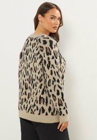 Beżowy sweter w cętki z czarnymi i brązowymi plamami, o luźnym kroju i prążkowanym dole, pokazany pod kątem z białym tłem.